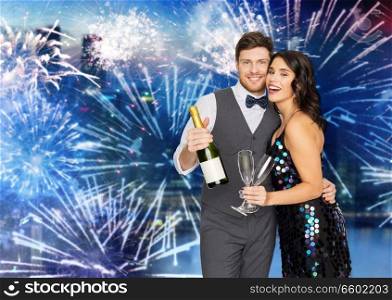 celebration and holidays concept - happy couple with bottle of non alcoholic champagne and wine glasses at party over firework background. happy couple with champagne and glasses at party