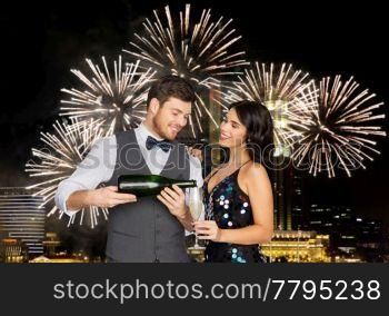 celebration and holidays concept - happy couple with bottle of non alcoholic champagne and wine glass at party over firework lights at night city background. happy couple with champagne and glass at party