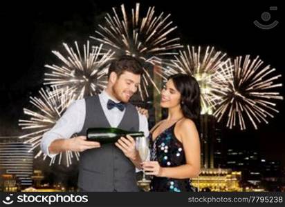 celebration and holidays concept - happy couple with bottle of non alcoholic champagne and wine glass at party over firework lights at night city background. happy couple with champagne and glass at party