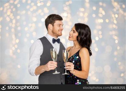 celebration and holidays concept - happy couple with glasses drinking non alcoholic champagne at party over festive lights background. happy couple with champagne glasses at party