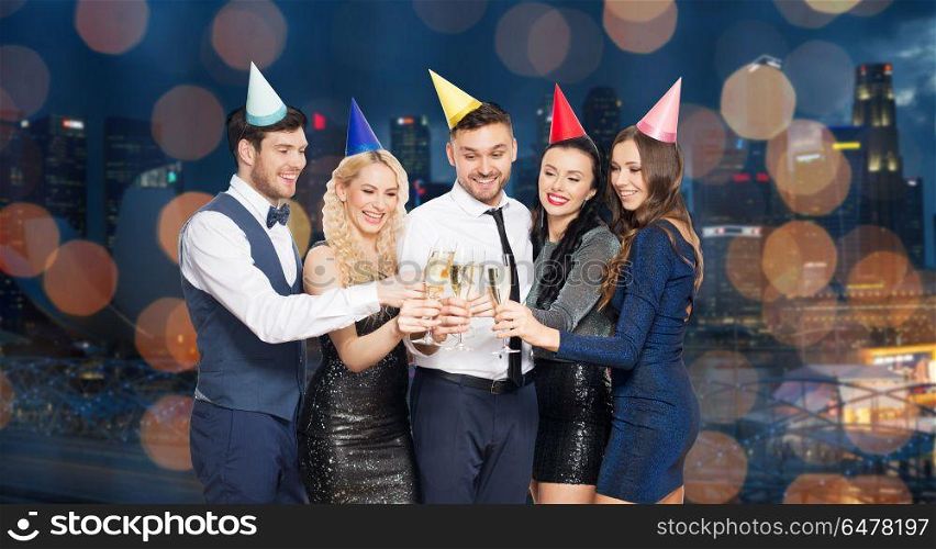 celebration and holidays concept - happy friends clinking champagne glasses at birthday party over night singapore city and lights background. friends with champagne glasses at birthday party. friends with champagne glasses at birthday party
