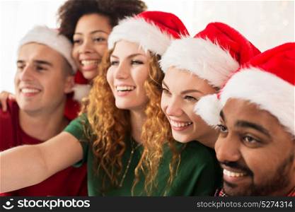 celebration and holidays concept - happy friends in santa hats taking selfie at christmas party. happy friends in santa hats at christmas party