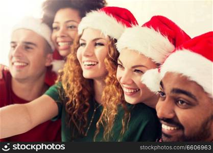 celebration and holidays concept - happy friends in santa hats taking selfie at christmas party. happy friends in santa hats at christmas party