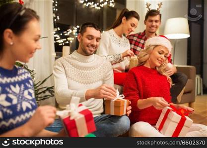 celebration and holidays concept - happy friends with glasses celebrating christmas at home party and opening presents. friends celebrating christmas and opening presents