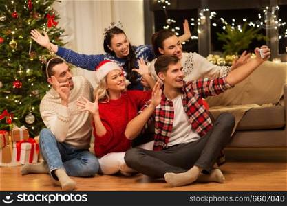 celebration and holidays concept - happy friends with glasses celebrating christmas at home party and taking selfie by smartphone. friends celebrating christmas and taking selfie