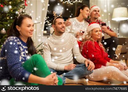 celebration and holidays concept - happy friends with glasses celebrating christmas at home party and drinking red wine over snow. friends celebrating christmas and drinking wine