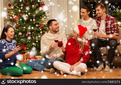celebration and holidays concept - happy friends with glasses celebrating christmas at home party and drinking red wine over snow. friends celebrating christmas and drinking wine