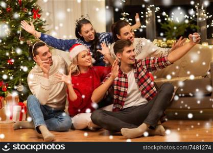 celebration and holidays concept - happy friends with glasses celebrating christmas at home party and taking selfie by smartphone over snow. friends celebrating christmas and taking selfie