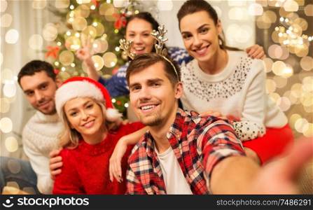 celebration and holidays concept - happy friends with glasses celebrating christmas at home party and taking selfie. friends celebrating christmas and taking selfie