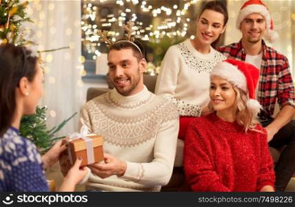 celebration and holidays concept - happy friends with glasses celebrating christmas at home party and giving presents. friends celebrating christmas and giving presents