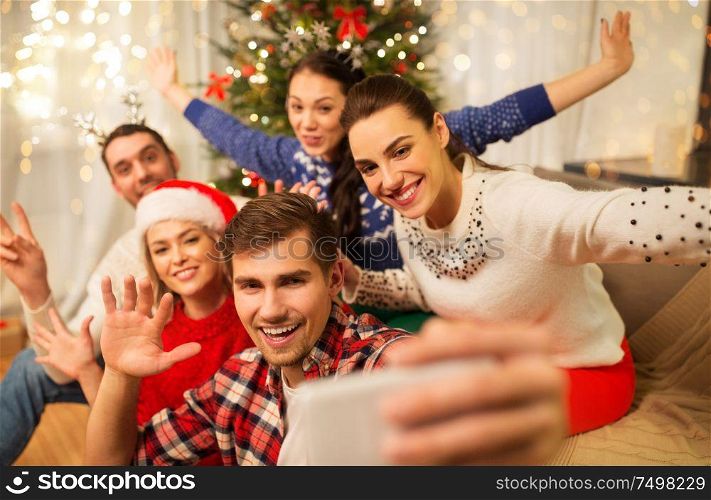 celebration and holidays concept - happy friends with glasses celebrating christmas at home party and taking selfie by smartphone. friends celebrating christmas and taking selfie