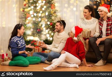 celebration and holidays concept - happy friends with glasses celebrating christmas at home party and giving presents. friends celebrating christmas and giving presents