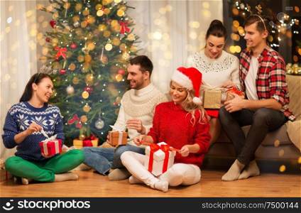 celebration and holidays concept - happy friends with glasses celebrating christmas at home party and opening presents. friends celebrating christmas and opening presents
