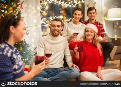 celebration and holidays concept - happy friends with glasses celebrating christmas at home party and drinking red wine. friends celebrating christmas and drinking wine
