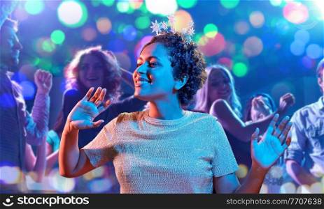 celebration and nightlife concept - happy smiling young african american woman dancing at christmas or new year party in ultraviolet neon lights over nightclub background. african woman dancing at party at nightclub