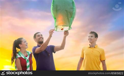 celebration and people concept - group happy friends lighting chinese sky lantern outdoors. happy friends lighting chinese sky lantern