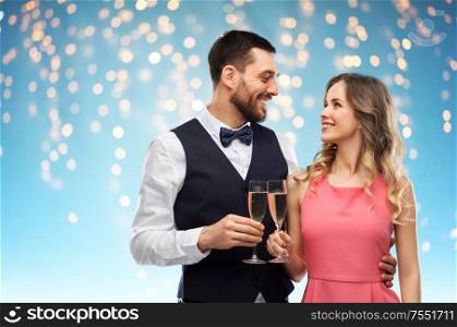 celebration and people concept - happy couple with champagne glasses toasting over holiday lights on blue background. happy couple with champagne glasses toasting