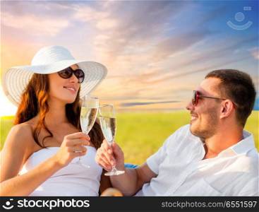 celebration and people concept - smiling couple drinking champagne on picnic over evening sky background. smiling couple drinking champagne on picnic. smiling couple drinking champagne on picnic