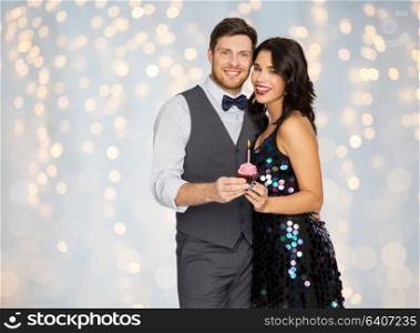 celebration, anniversary and holidays concept - happy couple with cupcake at birthday party over festive lights background. happy couple with cupcake at birthday party
