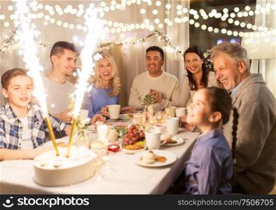 celebration, birthday and people concept - happy family having dinner party with fountain fireworks or sparkler candles burning on cake at home. happy family having dinner party at home