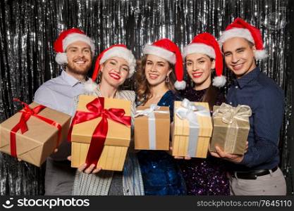 celebration, christmas and holiday concept - happy friends in santa hats with gifts at party. happy friends with gifts at christmas party