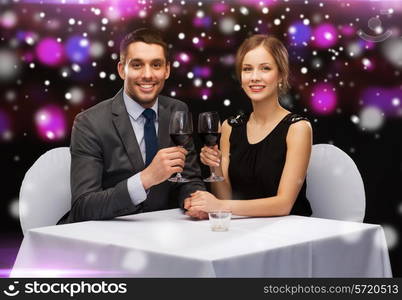 celebration, christmas, holidays and people concept - smiling couple clinking glasses of red wine at restaurant over night lights background