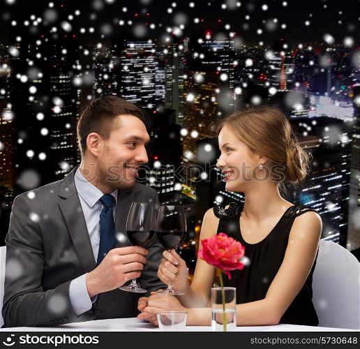 celebration, christmas, holidays and people concept - smiling couple clinking glasses of red wine at restaurant over snowy night city background