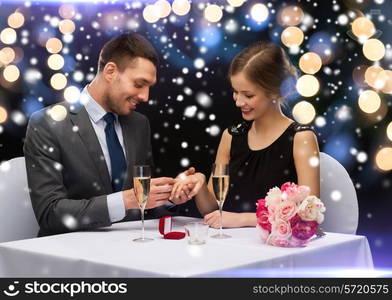 celebration, christmas, holidays and people concept - smiling couple with red gift box and ring at restaurant over night lights background