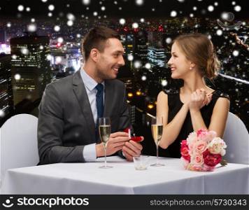 celebration, christmas, holidays and people concept - smiling couple with red gift box and ring at restaurant over snowy night city background