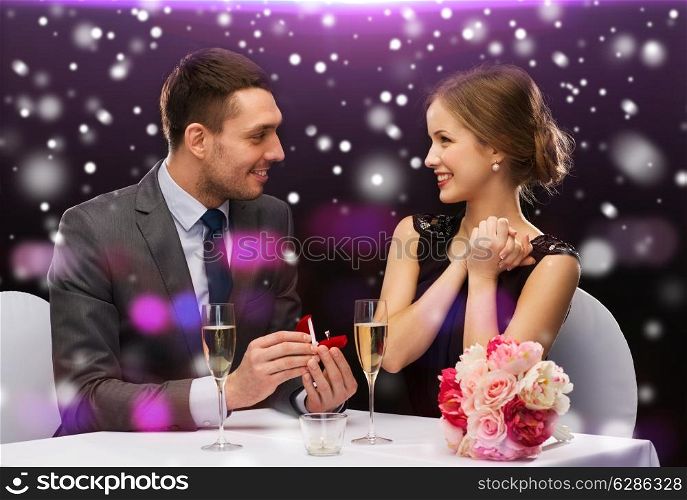 celebration, christmas, holidays and people concept - smiling couple with red gift box and ring at restaurant over night lights background