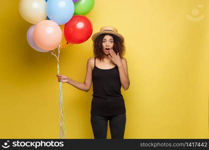 Celebration Concept - Close up Portrait happy young beautiful african woman in black t-shirt surprising with colorful party balloon. Yellow Pastel studio Background.. Celebration Concept - Close up Portrait happy young beautiful african woman in black t-shirt surprising with colorful party balloon. Yellow Pastel studio Background