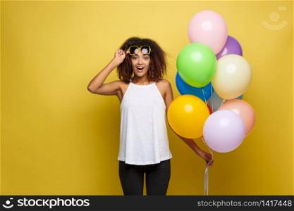Celebration Concept - Close up Portrait happy young beautiful african woman with white t-shirt surprising expression with colorful party balloon. Yellow Pastel studio Background.. Celebration Concept - Close up Portrait happy young beautiful african woman with white t-shirt surprising expression with colorful party balloon. Yellow Pastel studio Background