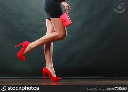 Celebration disco and evening fashion concept. Woman in black short dress red spiked shoes holding handbag purse, part of body female legs in high heels on party floor