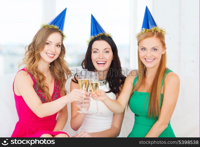 celebration, drinks, friends, bachelorette party, birthday concept - three smiling women wearing blue hats with champagne glasses