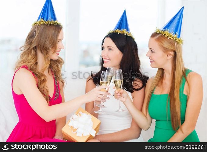 celebration, drinks, friends, bachelorette party, birthday concept - three smiling women wearing blue hats with champagne glasses and gift