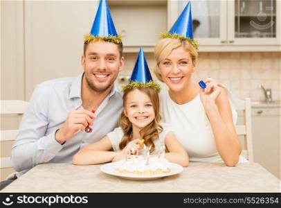celebration, family, holidays and birthday concept - happy family in blue hats with cake and candles blowing favor horns