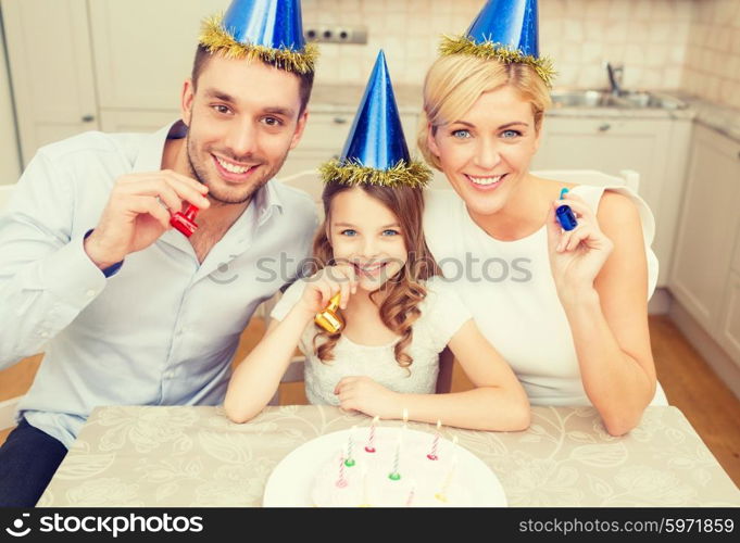 celebration, family, holidays and birthday concept - happy family in blue hats with cake and candles blowing favor horns