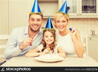 celebration, family, holidays and birthday concept - happy family in blue hats with cake and candles blowing favor horns