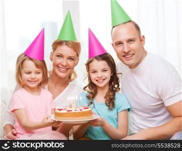 celebration, family, holidays and birthday concept - happy family with two kids in hats with cake at home