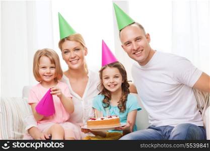 celebration, family, holidays and birthday concept - happy family with two kids in hats with cake at home