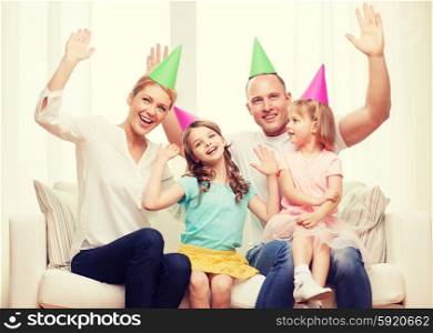 celebration, family, holidays, children and birthday concept - happy family with two chldren in hats waving hands at home