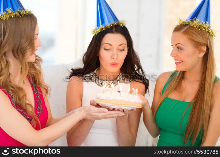 celebration, food, friends, bachelorette party, birthday concept - three smiling women wearing blue hats holding cake with candles