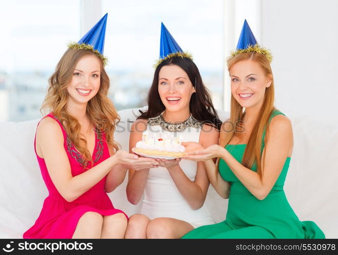 celebration, food, friends, bachelorette party, birthday concept - three smiling women wearing blue hats holding cake with candles