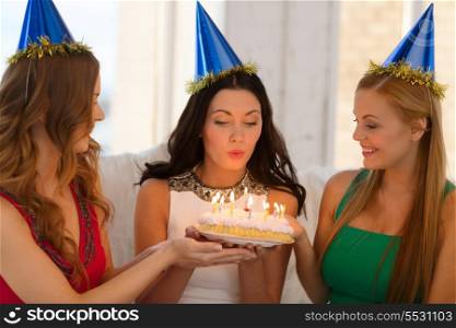 celebration, food, friends, bachelorette party, birthday concept - three smiling women wearing blue hats holding cake with candles