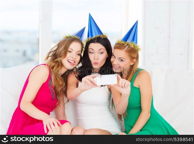 celebration, friends, bachelorette party, birthday concept - three smiling women in blue hats having fun with smartphone photo camera