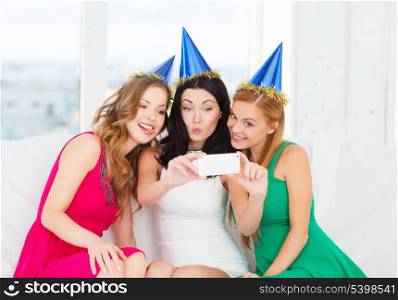 celebration, friends, bachelorette party, birthday concept - three smiling women in blue hats having fun with smartphone photo camera