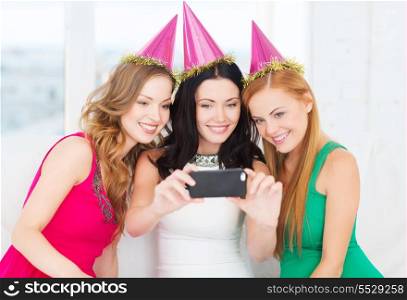 celebration, friends, bachelorette party, birthday concept - three smiling women in pink hats having fun with smartphone photo camera