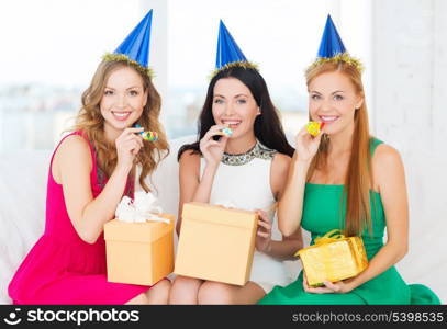 celebration, friends, bachelorette party, birthday concept - three smiling women wearing blue hats with gift boxes blowing favor horns