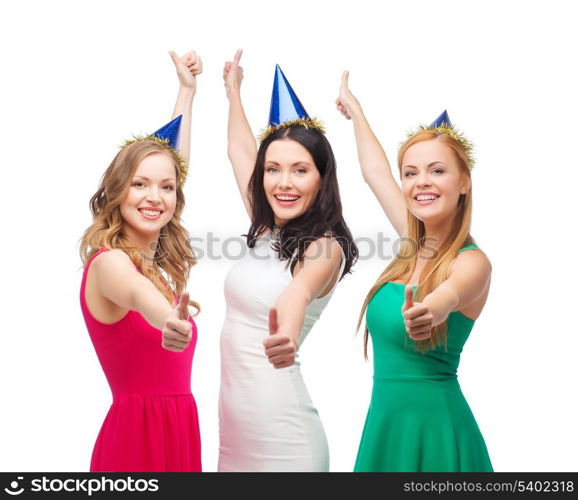 celebration, friends, bachelorette party, birthday concept - three smiling women wearing blue hats and showing thumbs up