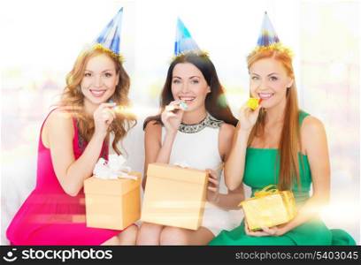 celebration, friends, bachelorette party, birthday concept - three smiling women wearing blue hats with gift boxes blowing favor horns